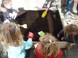 Met schepjes en harkjes helpen de kinderen van ’t Schommeltje met het vullen van hun moestuinbak. 