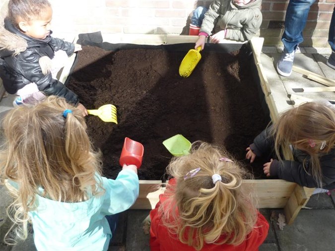 Met schepjes en harkjes helpen de kinderen van ’t Schommeltje met het vullen van hun moestuinbak. 